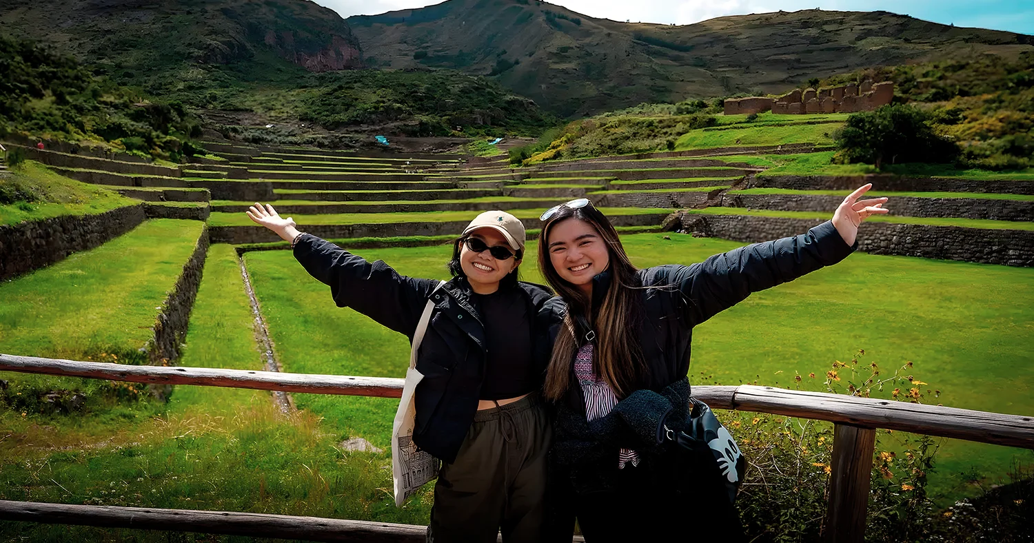 Two travelers posing in front of the green agricultural terraces at Tipon archaeological site in Cusco