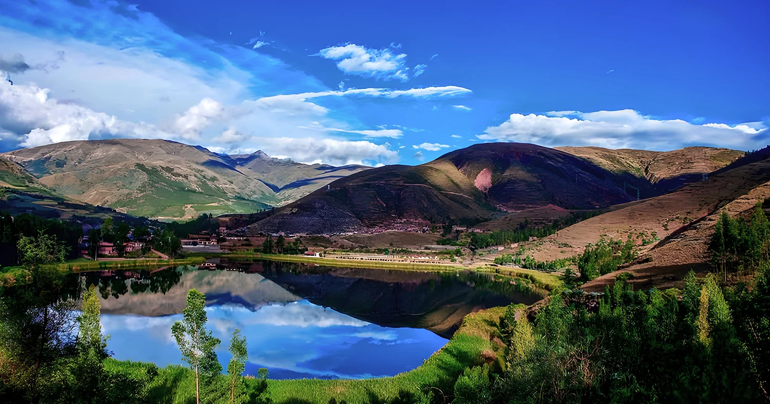 Panoramic view of Urcos Lake reflecting the surrounding Andean hills and blue sky near Cusco, Peru