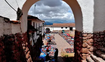 Traditional handicraft market in Chinchero, Cusco, with colorful Andean textiles displayed beneath a colonial arch
