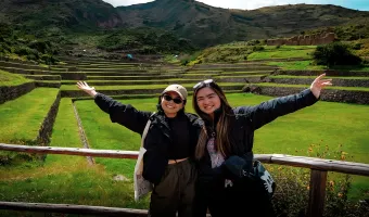 Two travelers posing in front of the green agricultural terraces at Tipon archaeological site in Cusco