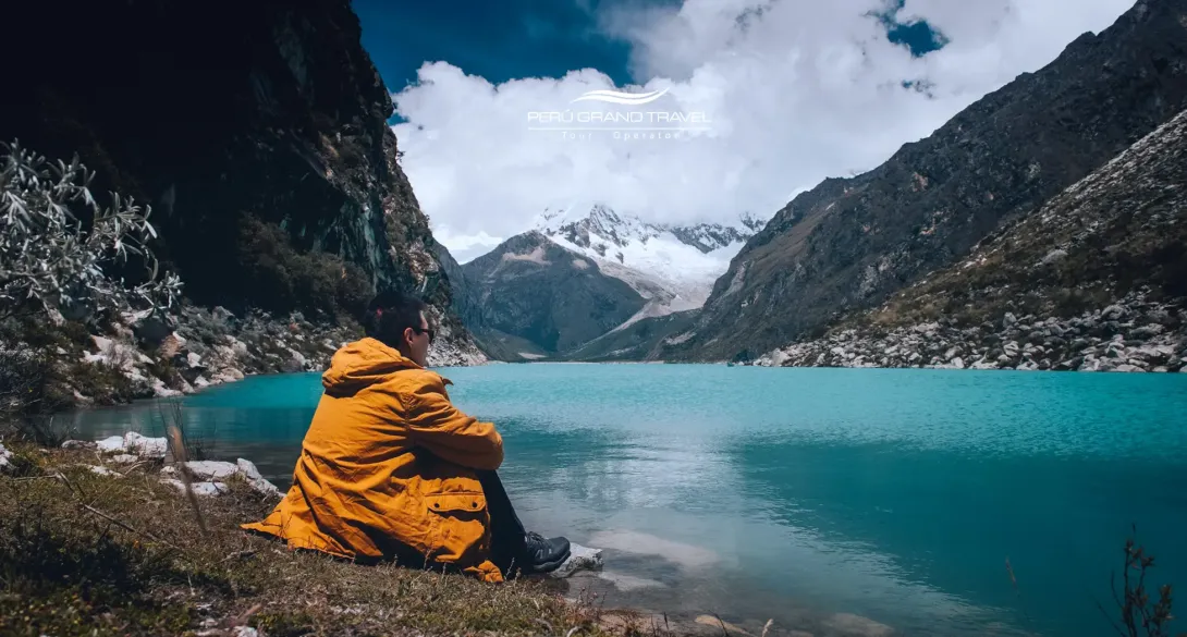 Traveler sitting on a mountaintop overlooking clouds and a turquoise lake, illustrating how high is Huaraz Peru at 3,052 meters.