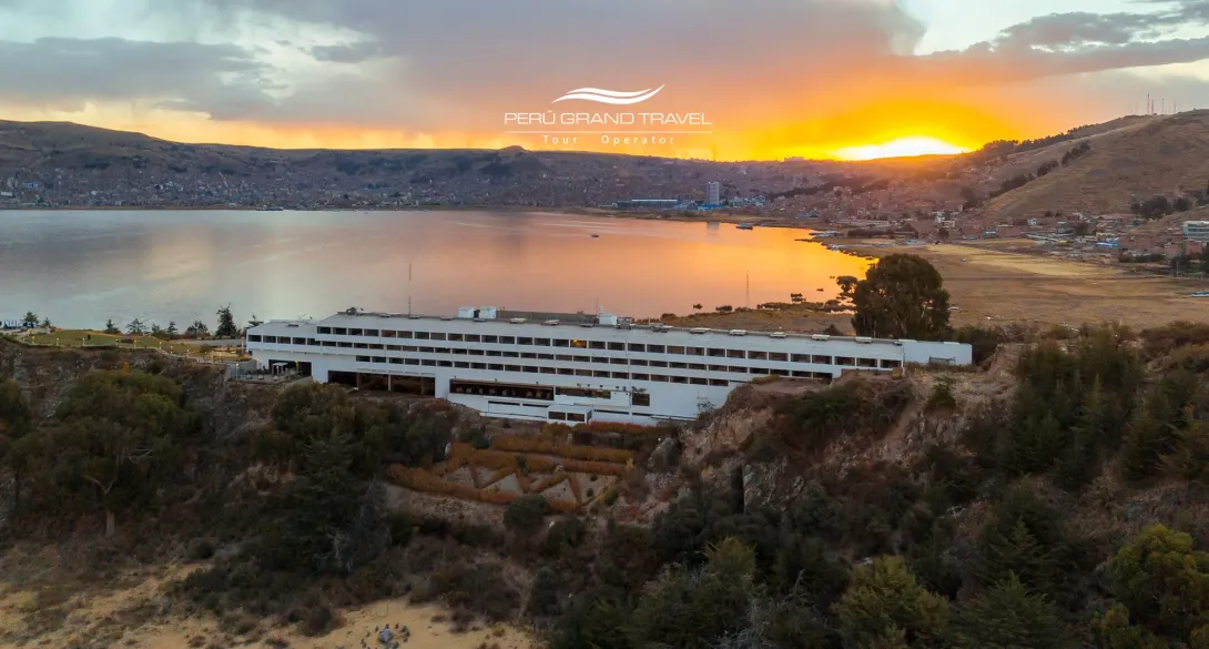 Luxury Hotels in Puno: panoramic sunset view of a lakefront hotel on Lake Titicaca with Puno city in the background.